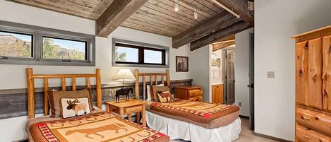 Un dormitorio con dos camas, cabeceros de madera, una mesita de noche, una lámpara y un armario de madera.