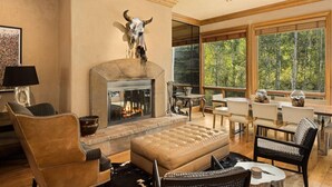 A spacious living room with a fireplace, comfortable seating, and large windows offering a view of the forest. - Owl Creek 20 | Luxury family home with private balcony, deck, hot tub, and patio - near lifts! (Snowmass Village)