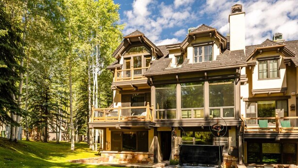 A large, multi-story house with a stone fireplace, multiple balconies, and a well-maintained lawn. - Owl Creek 20 | Luxury family home with private balcony, deck, hot tub, and patio - near lifts! (Snowmass Village)