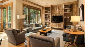 A spacious living room with a large TV, comfortable seating, and wooden paneling. - Owl Creek 20 | Luxury family home with private balcony, deck, hot tub, and patio - near lifts! (Snowmass Village)