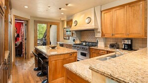 A spacious kitchen with wooden cabinets, granite countertops, and a central island with bar stools. - Owl Creek 20 | Luxury family home with private balcony, deck, hot tub, and patio - near lifts! (Snowmass Village)