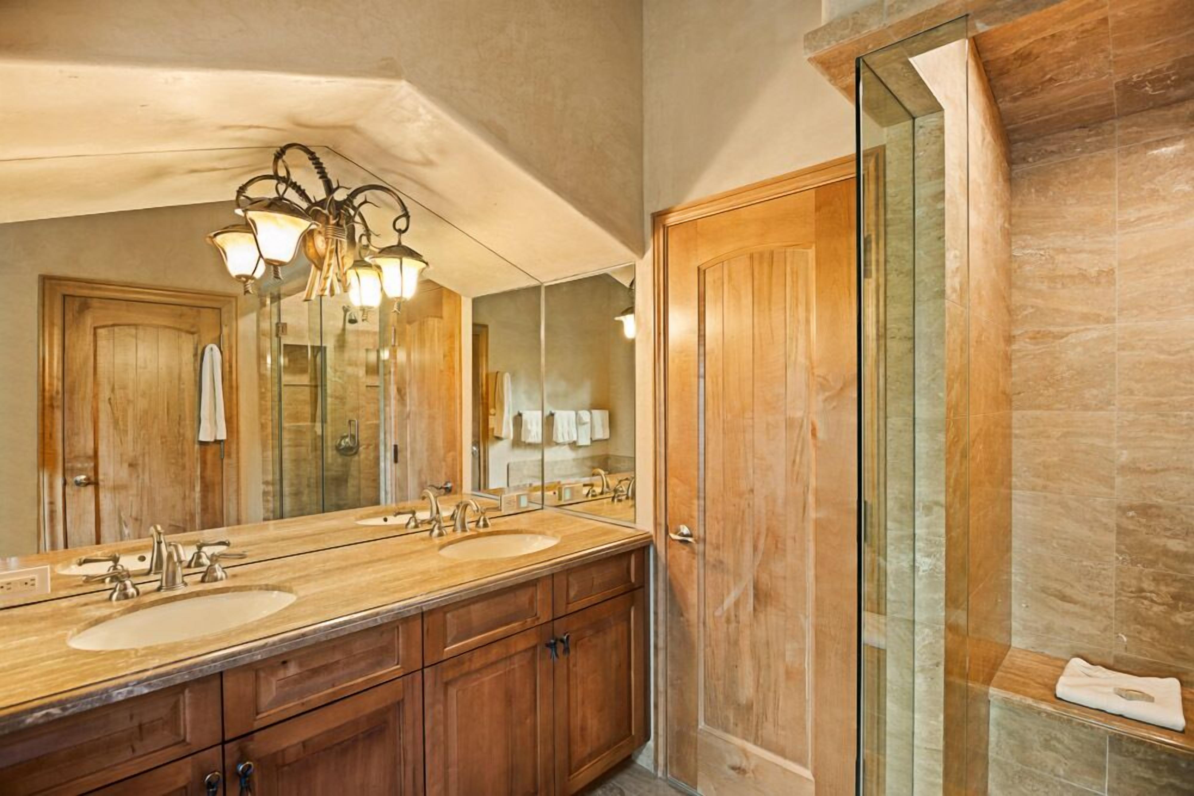 A bathroom with a large mirror, two sinks, wooden cabinets, and a shower area.