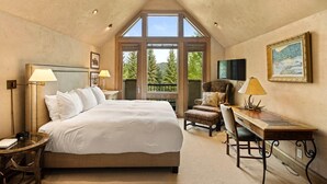 A bedroom with a large bed, a desk, and a chair, a window with a view of trees, and a painting on the wall. - Owl Creek 20 | Luxury family home with private balcony, deck, hot tub, and patio - near lifts! (Snowmass Village)