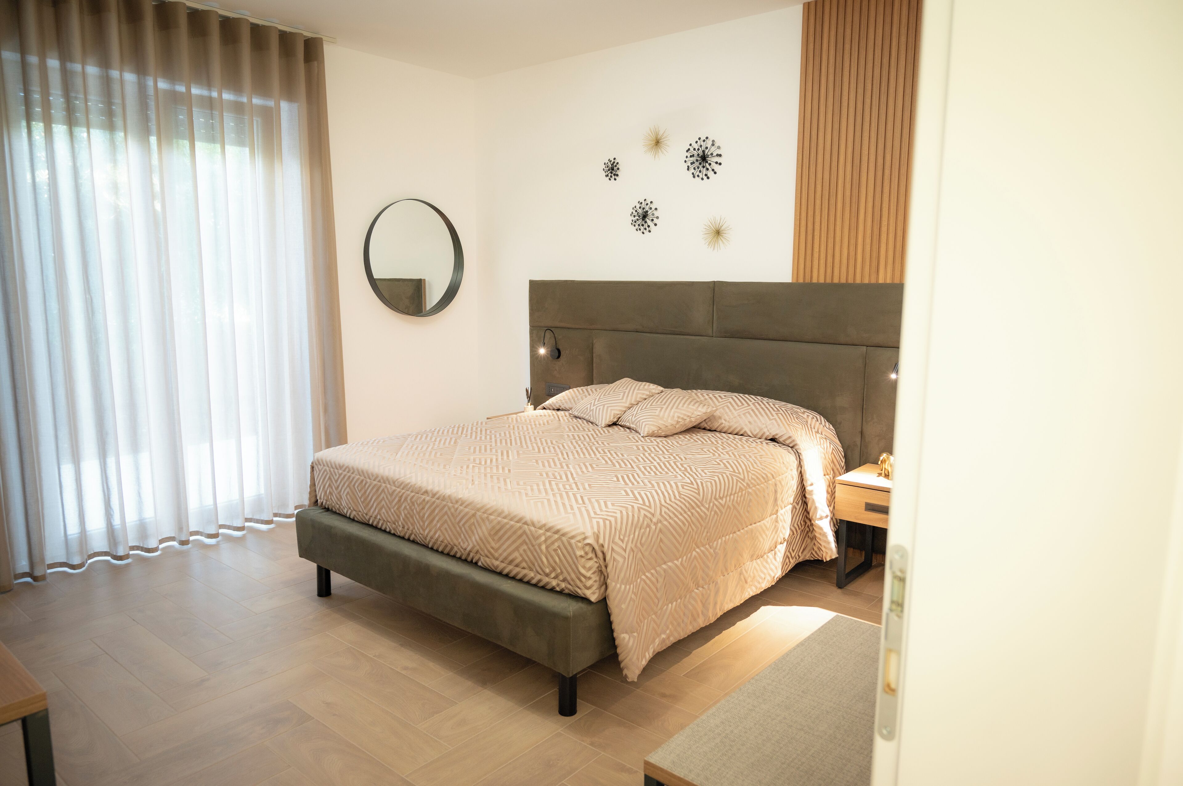 A modern bedroom with a large bed, a bedside table, a mirror, and decorative wall art.