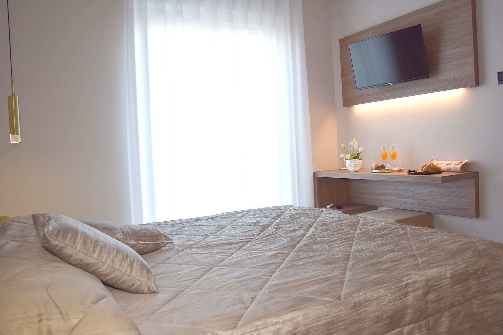 Une chambre à coucher avec un lit, un téléviseur fixé au mur et une table de chevet sur laquelle se trouvent une lampe et une petite plante.