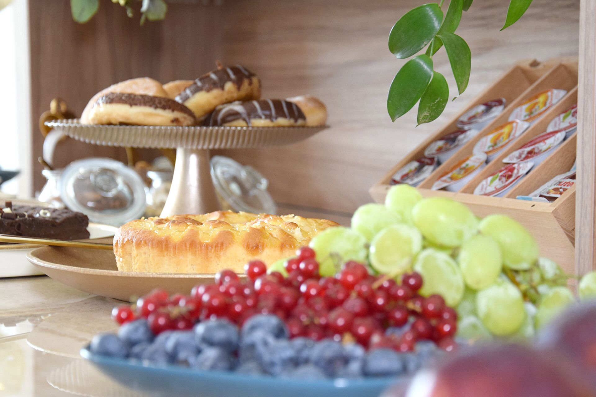 Una mesa con una variedad de pasteles, incluyendo un pastel grande cubierto de fruta, y una selección de frutas frescas como uvas y bayas.