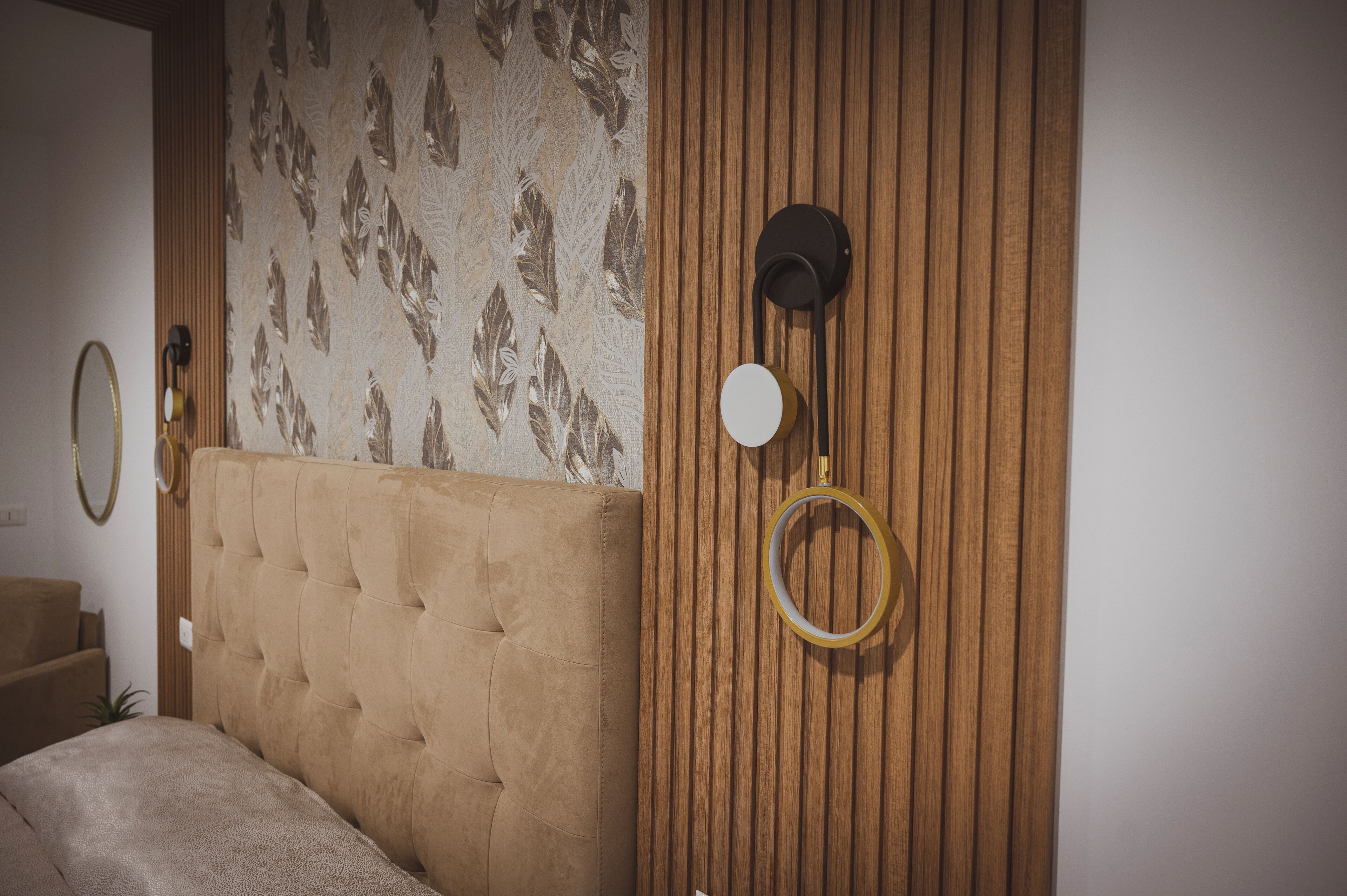 Une chambre à coucher avec une tête de lit capitonnée, un mur recouvert de panneaux en bois et un miroir avec un cadre doré.