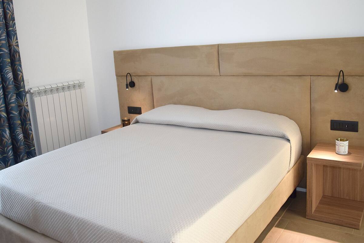 Ein ordentlich gemachtes Bett mit einem hölzernen Kopfteil, zwei Nachttischlampen und einem kleinen Nachttisch mit einer Tasse.