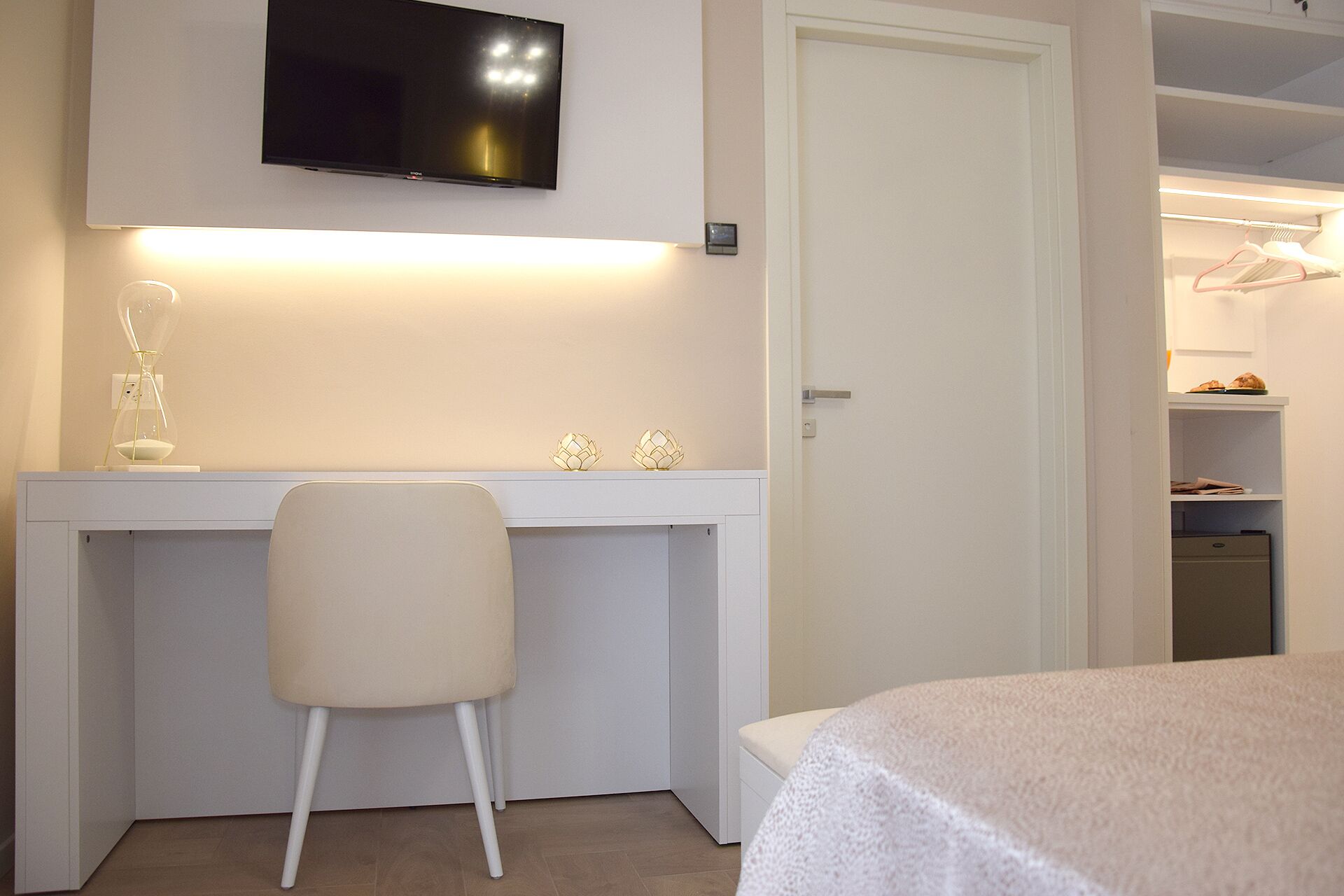 Ein Schlafzimmer mit Bett, Schreibtisch mit Stuhl, einem an der Wand befestigten Fernseher und einem Kleiderschrank mit Kleidung.