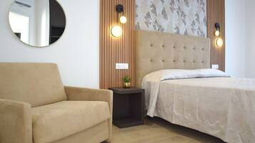 Un dormitorio con cama, una silla, un espejo redondo e iluminación en la pared.