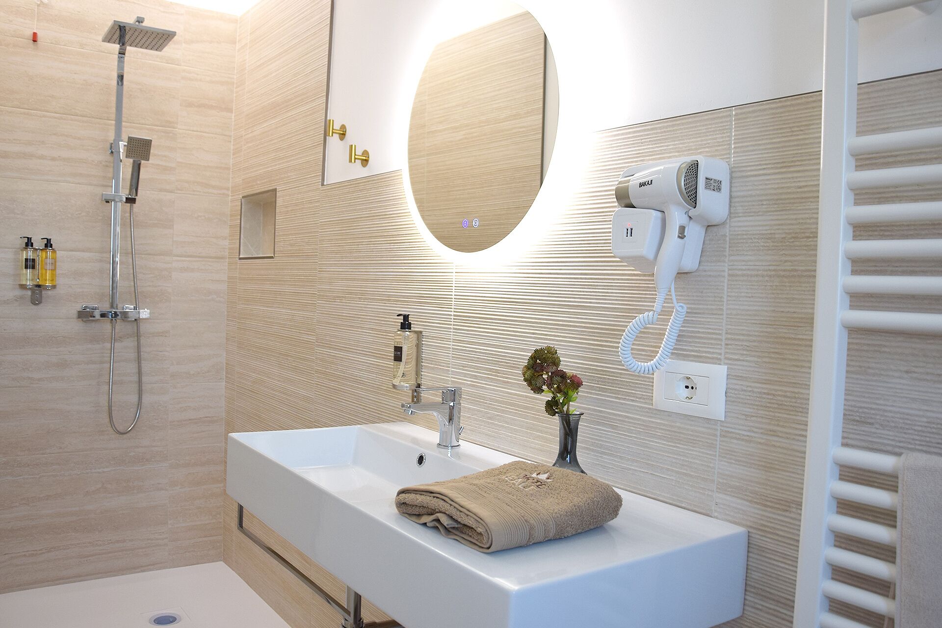 Un baño moderno con un lavamanos grande, un cabezal de ducha de mano, un secador de pelo y una toalla sobre el mostrador.