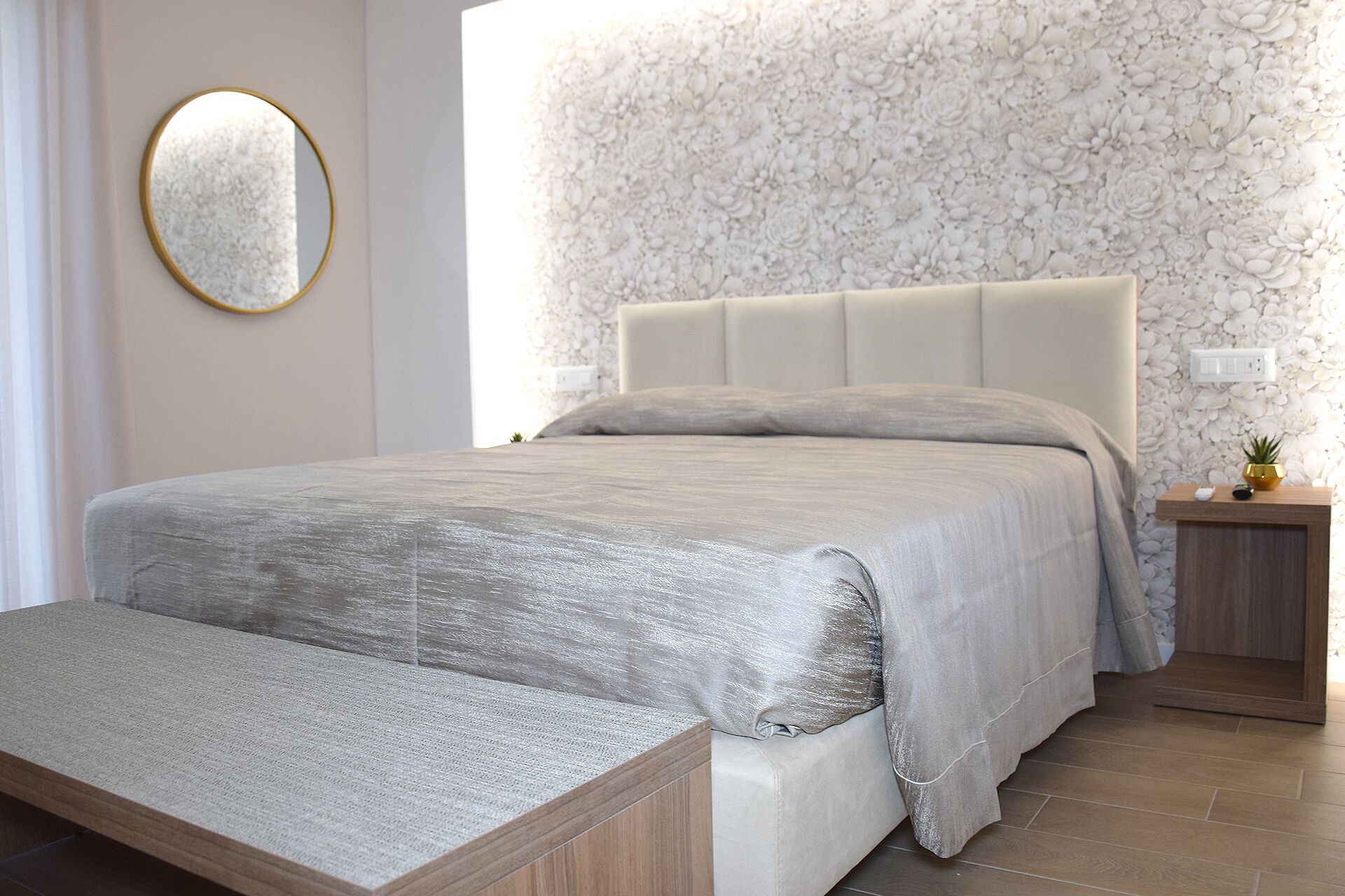 Un dormitorio con una cama grande, una mesita de noche con lámpara y un papel tapiz estampado con flores.