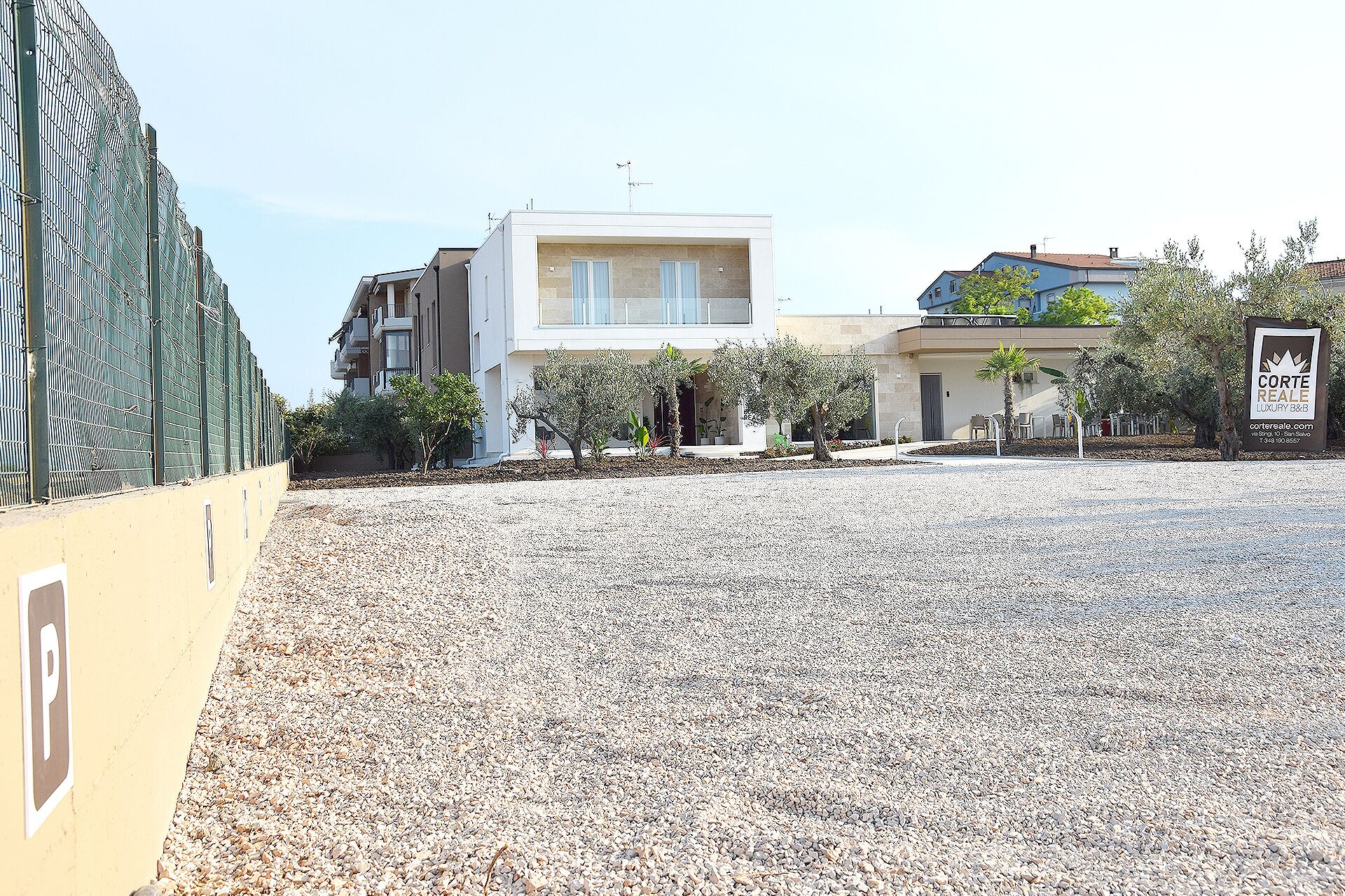 A modern building with a flat roof, a gravel driveway, and a signboard for Corte Real Estate.