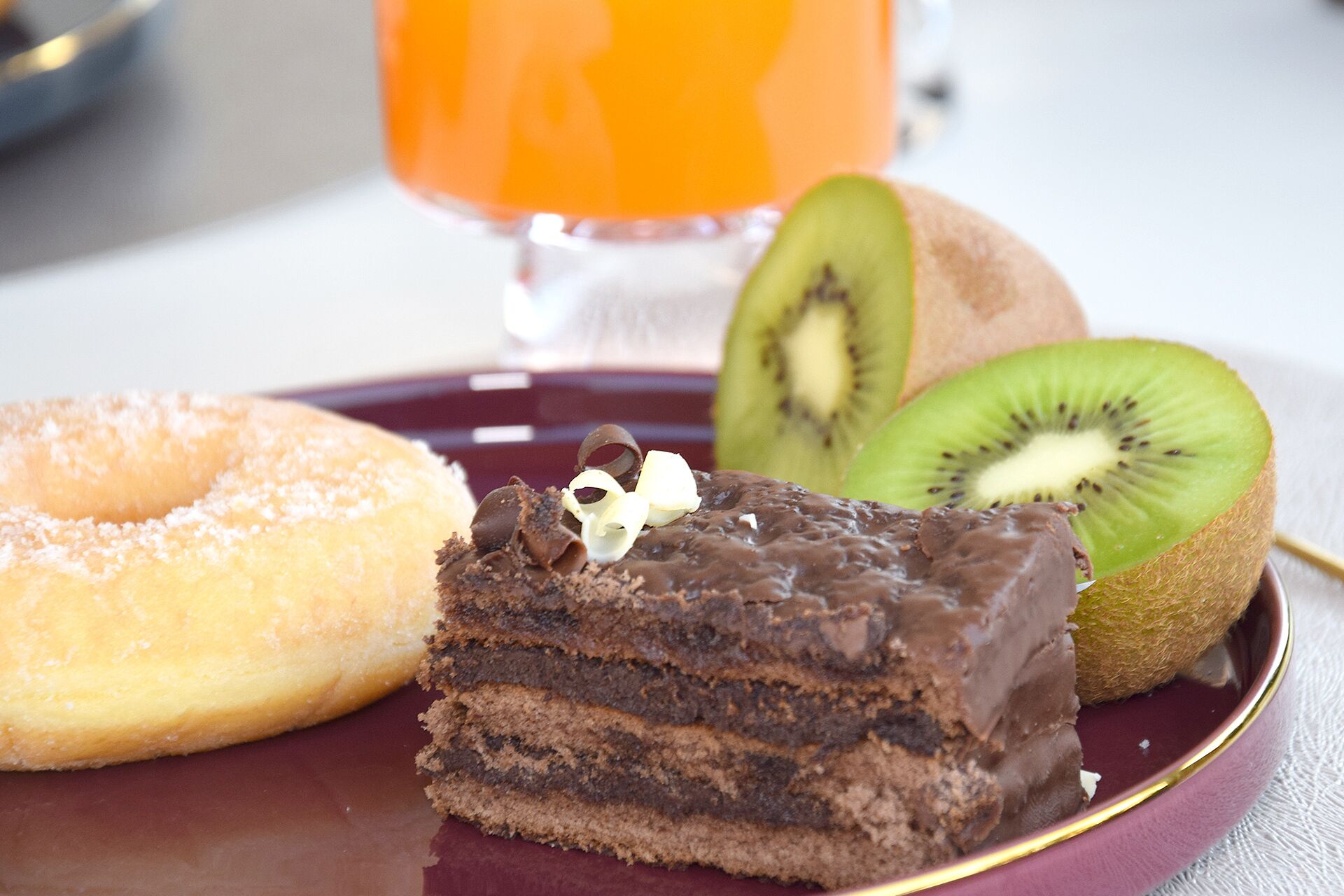 A dessert plate with a slice of chocolate cake, a donut, and a kiwi slice.