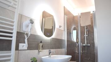 A modern bathroom with a white sink, a hairdryer, a mirror, and a glass-enclosed shower.