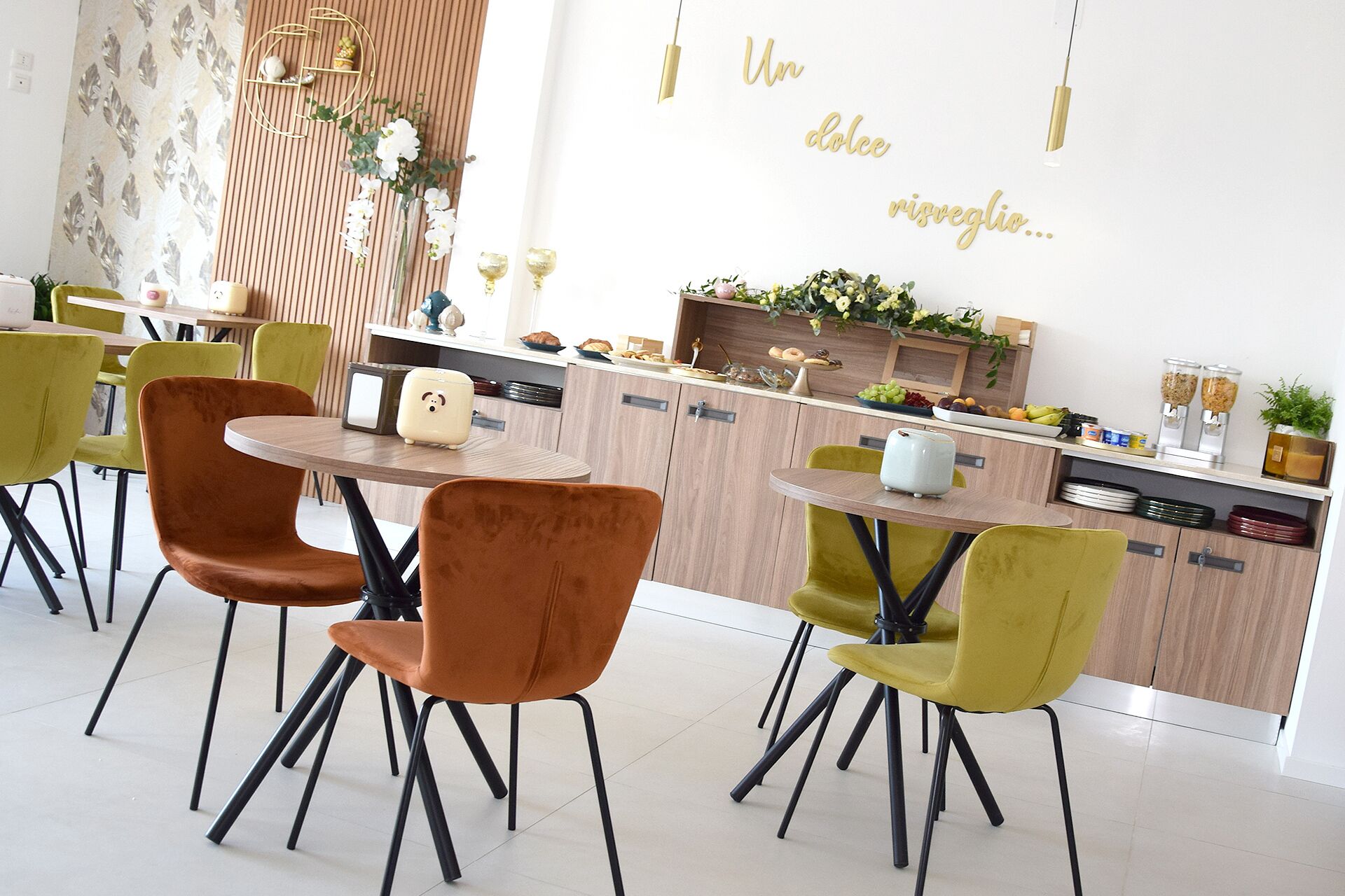 A modern dining area with a wooden counter, green and brown chairs, and a decorative wall with a phrase in gold lettering.