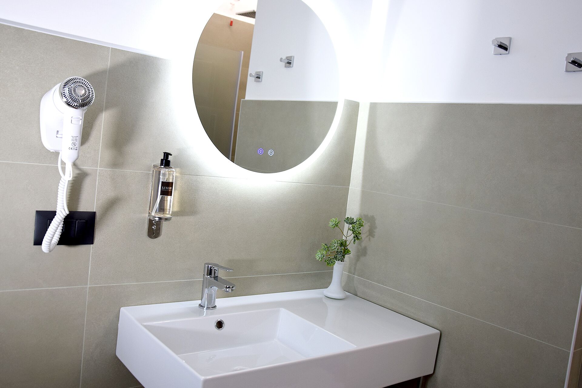 Un bagno con un lavandino bianco, uno specchio, un asciugacapelli e una bottiglia di lozione.