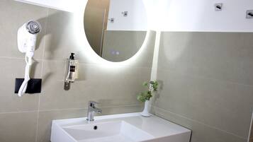 Un bagno con un lavandino bianco, uno specchio, un asciugacapelli e una bottiglia di lozione.
