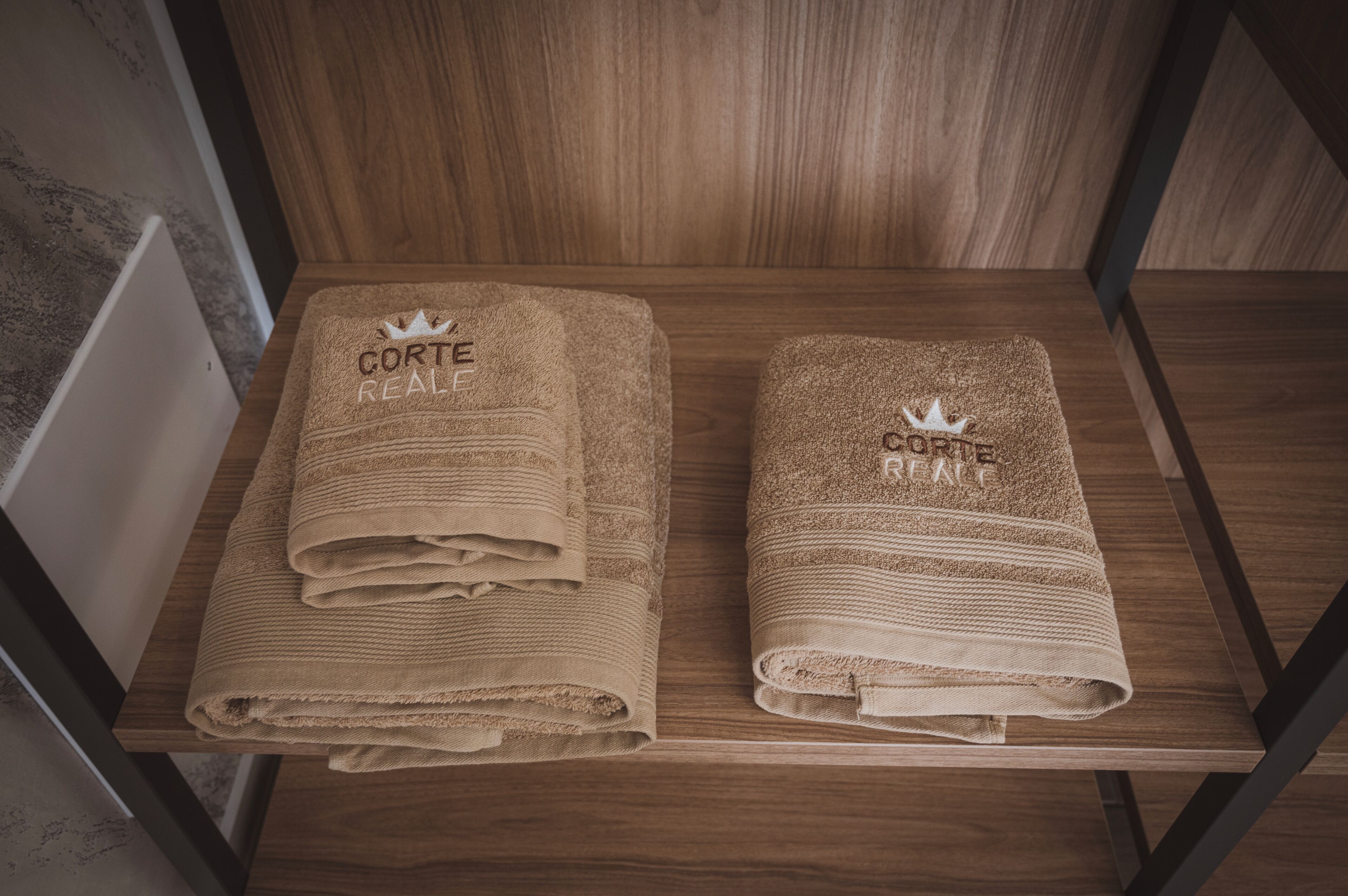 Two neatly folded towels with the text "Corte Real" and a crown symbol on a wooden shelf.
