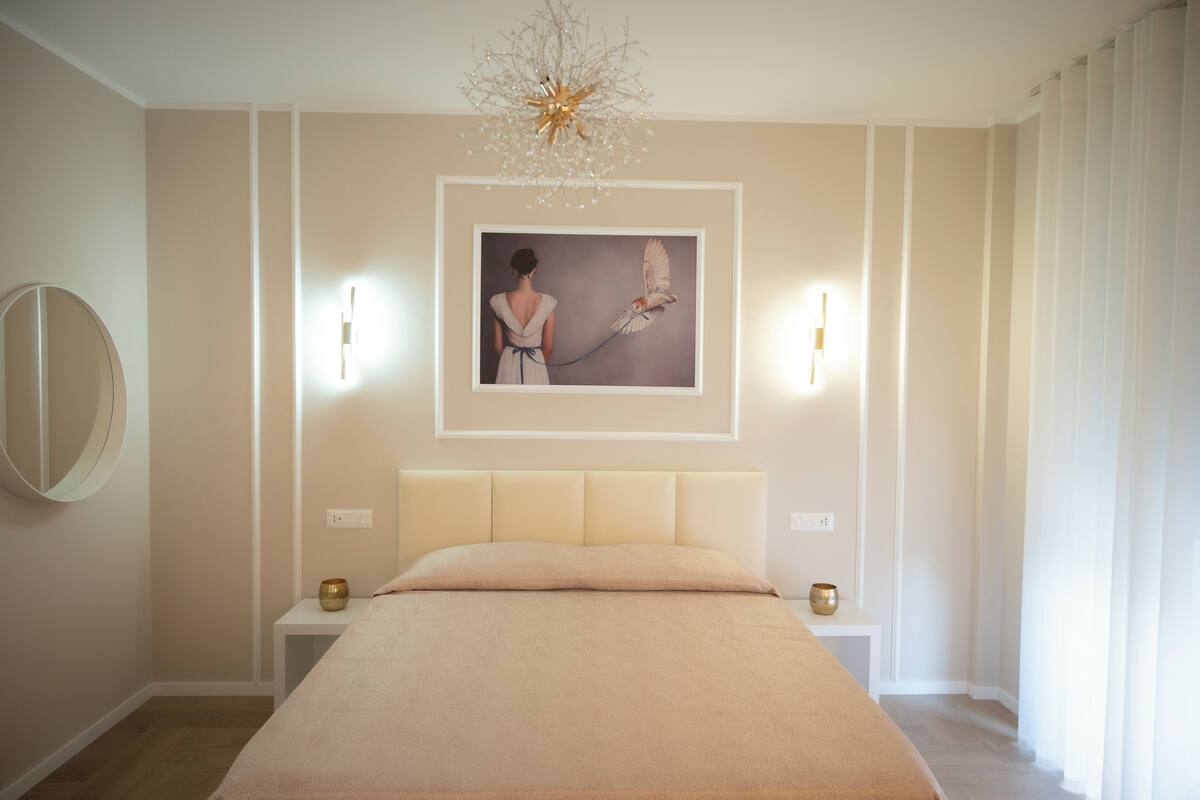 Ein Schlafzimmer mit einem großen Bett, einem gerahmten Bild an der Wand, Nachttischen und einer Kronleuchter.