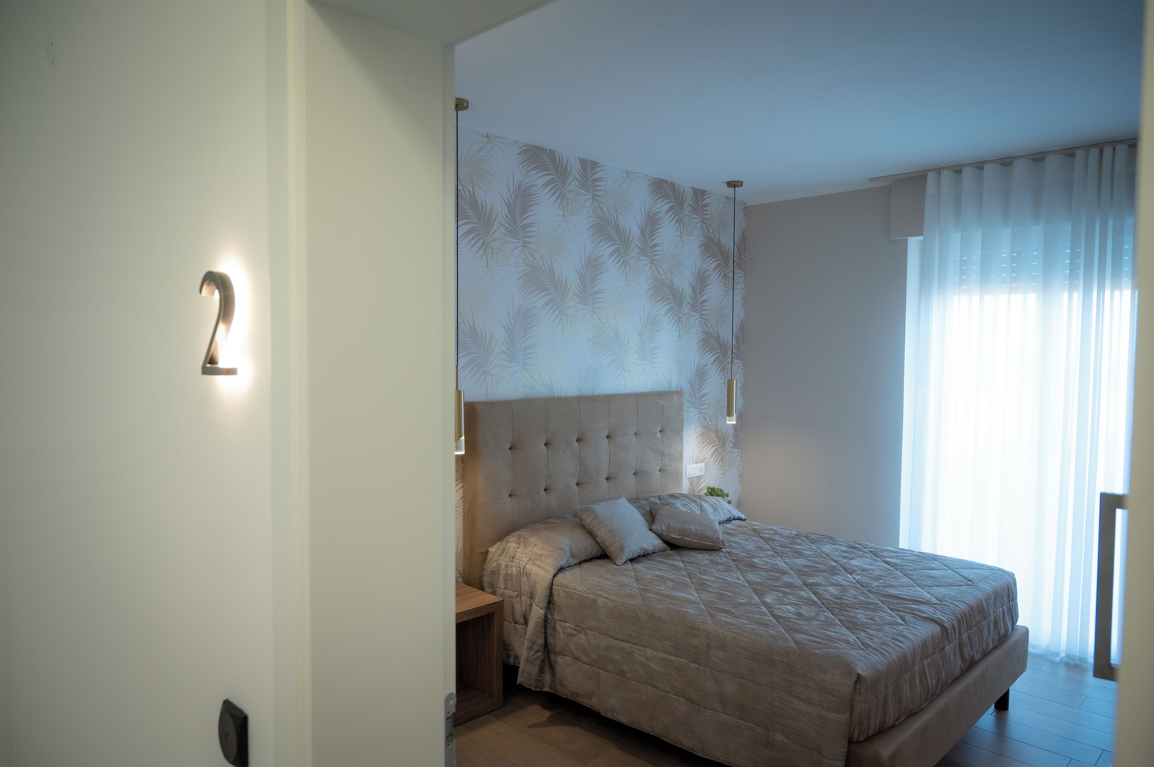 A bedroom with a large bed, a headboard with a leaf pattern, a nightstand, and a wall-mounted light.
