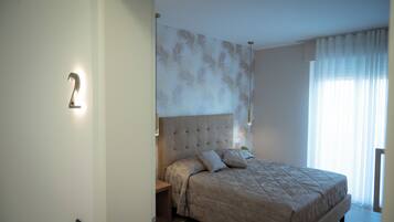 A bedroom with a large bed, a headboard with a leaf pattern, a nightstand, and a wall-mounted light.