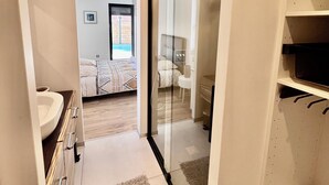 Ein modernes Badezimmer mit Duschabtrennung aus Glas, einem weißen Waschbecken und einem begehbaren Kleiderschrank mit Regalen.