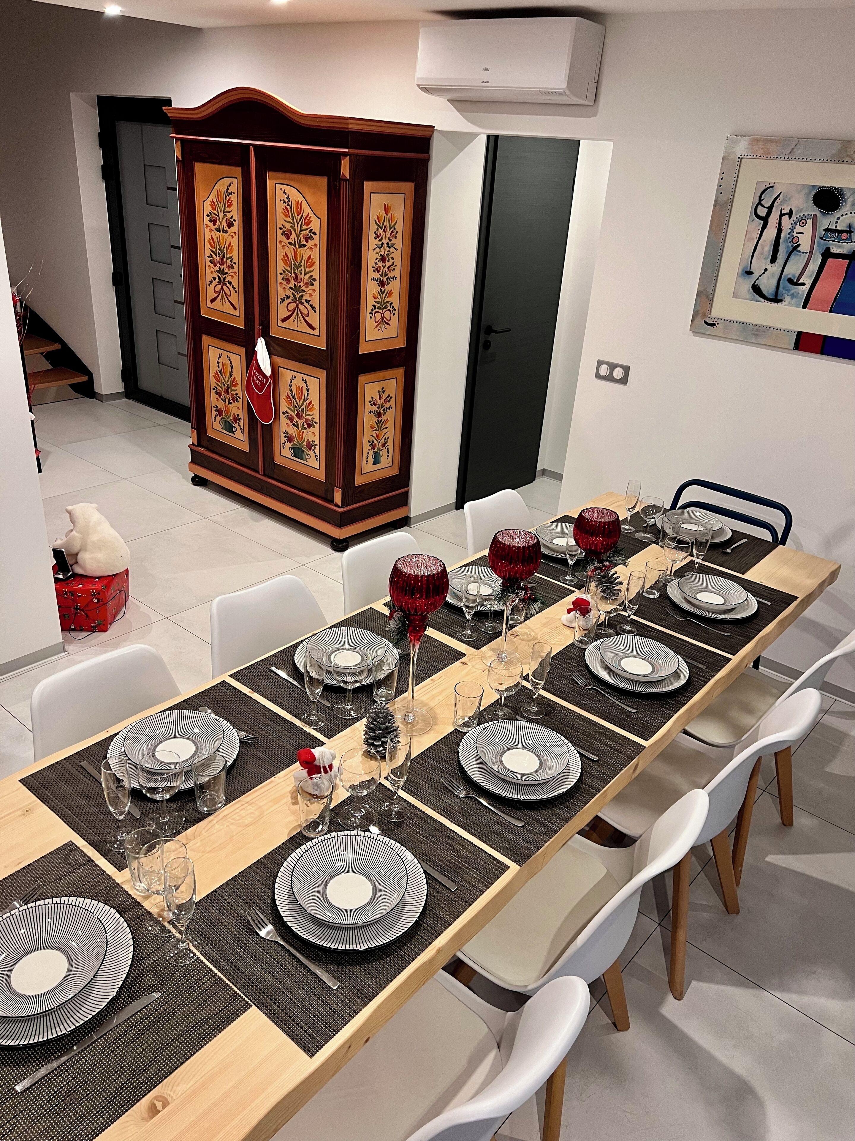 A dining area with a long table set for six, featuring black and white plates, red glassware, and a decorative centerpiece.