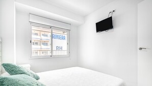 Et soveværelse med en seng, et vindue der ud til en bygning, og et ophængt TV.