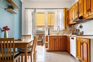 Eine Küche mit Holzausstattung, einem Esstisch mit Stühlen, einem Fenster mit Vorhängen und einer kleinen Pflanze auf einem Regal.