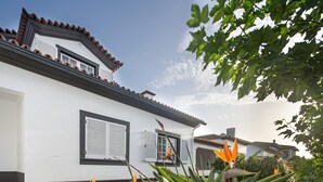A white building with a tiled roof, a balcony with a balustrade, and a window with shutters.