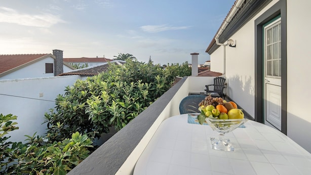 A balcony with a table, a bowl of fruit, and a view of neighboring buildings and greenery.