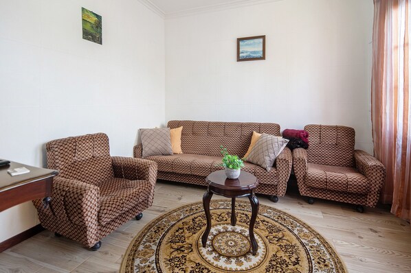 A living room with patterned furniture, a round table with a plant, and a decorative rug.