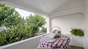 Une table dressée avec une nappe à carreaux, des chaises blanches et une plante en pot sur un balcon offrant une vue sur la verdure.