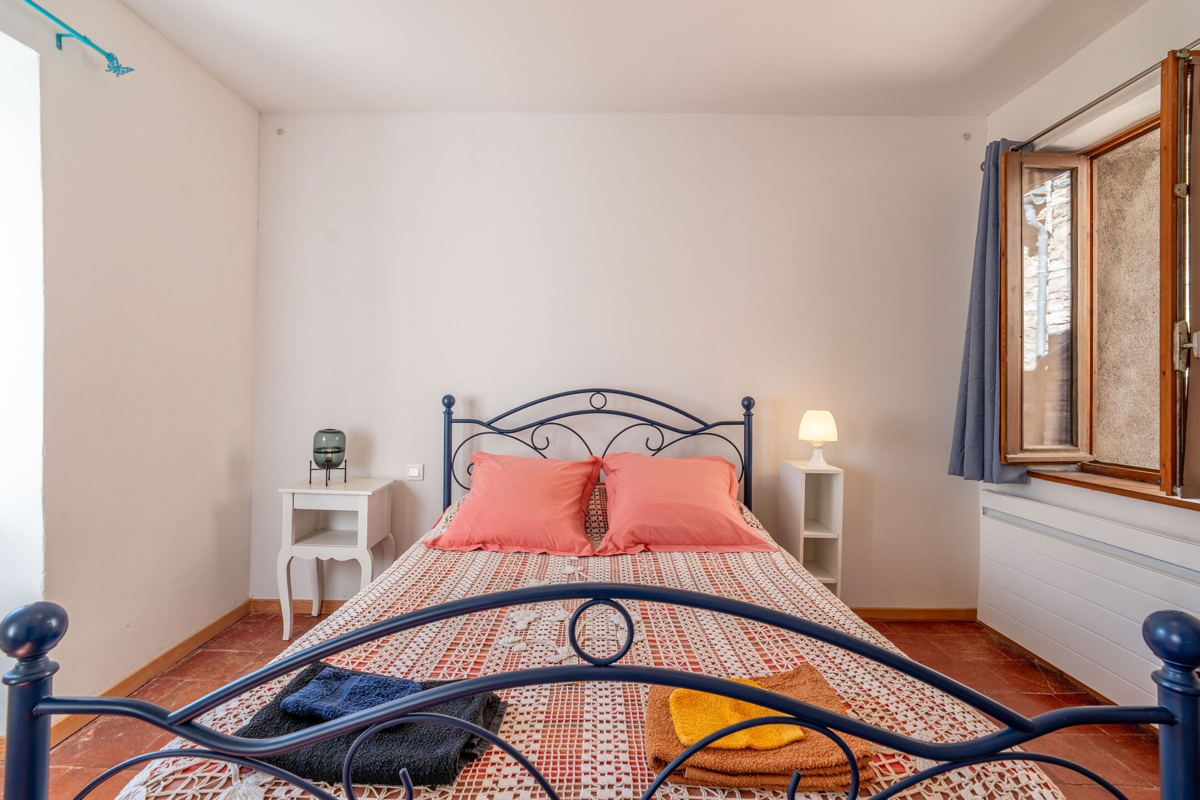 A bed with a metal frame, two bedside tables, a lamp, and a window with curtains.