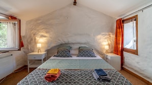 Alojamiento acogedor de una sola habitación con techo inclinado, cama con ropa de cama estampada, lámparas de noche y una ventana con cortinas.