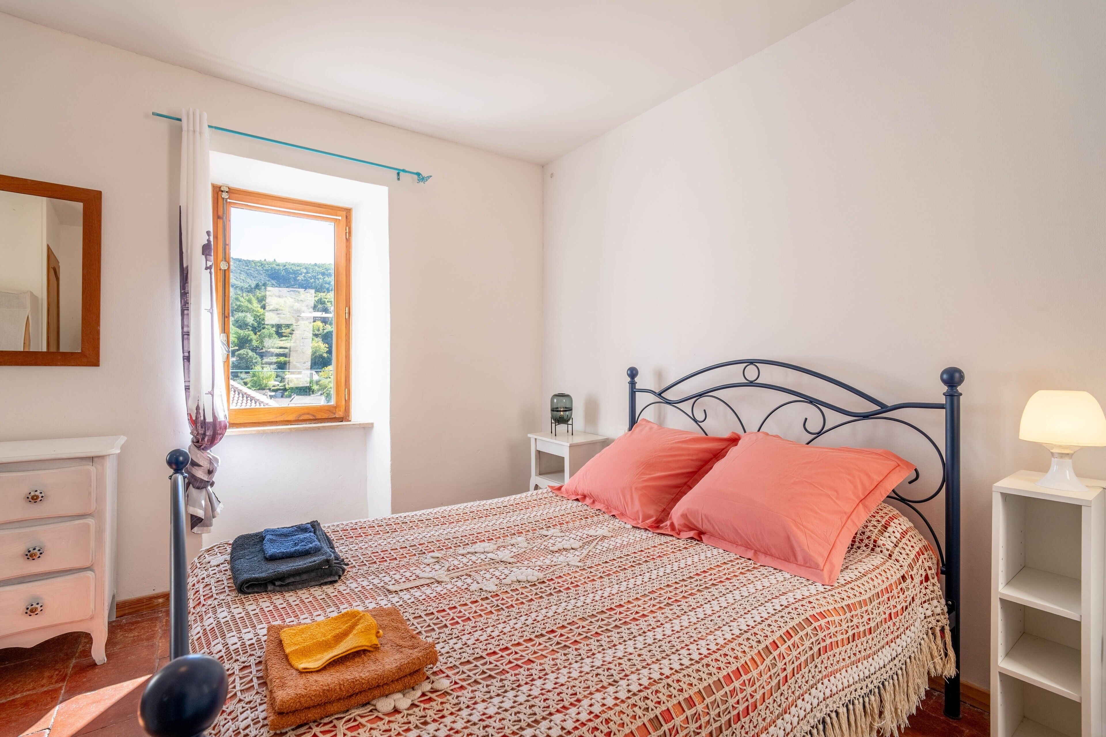 Un dormitorio con cama, mesita de noche, lámpara, cómoda y ventana con vistas.