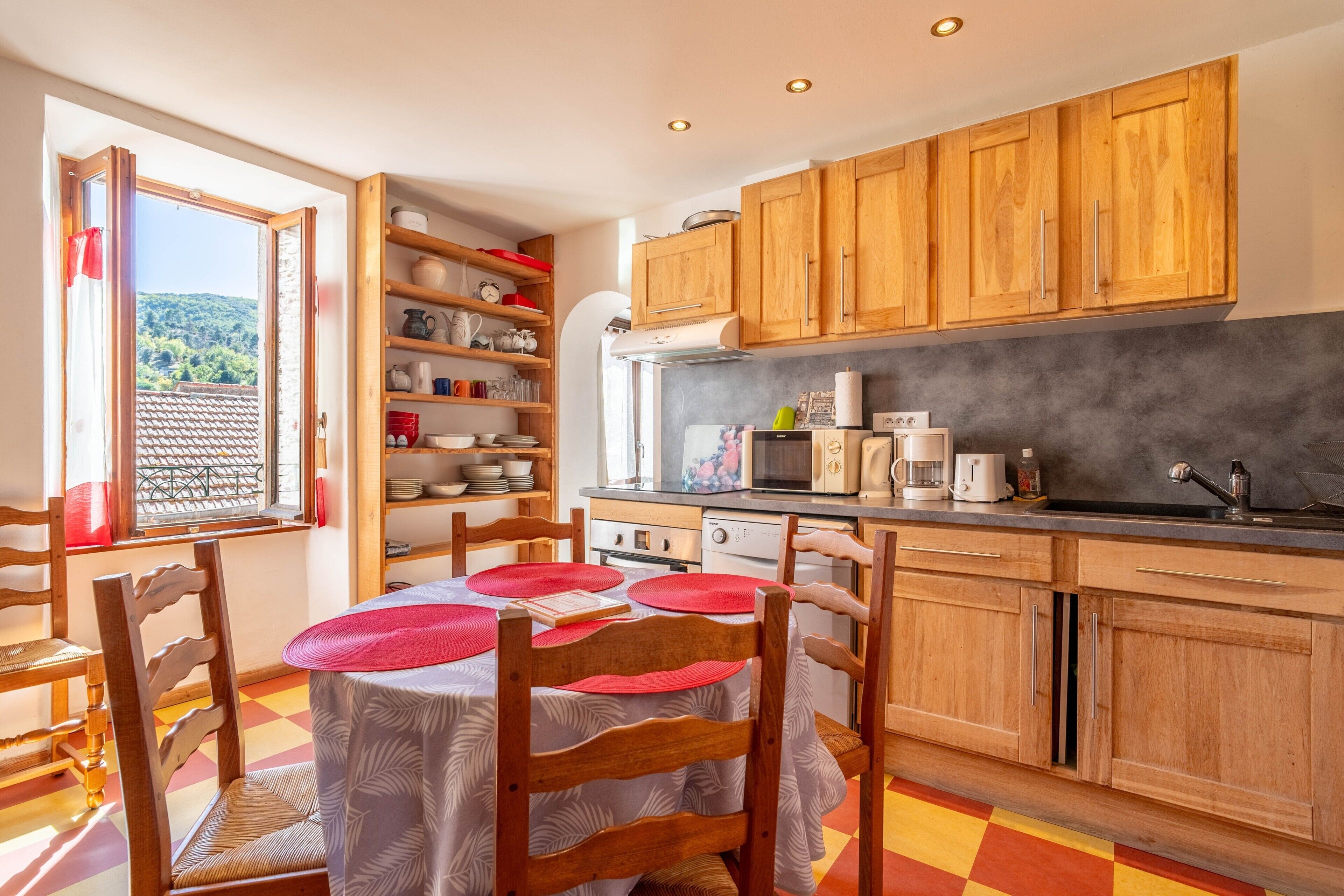 A kitchen with wooden cabinets, a dining table with chairs, and a view through an open door.