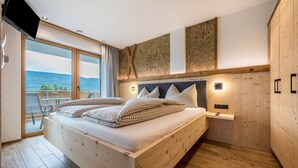 Ein Schlafzimmer mit Bett, Fernseher, Nachttisch und Blick ins Freie.
