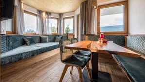 Ein gemütliches Interieur mit Holzbalkendecke, großen Fenstern, einem Holzessttisch und einer gepolsterten Sitzecke.