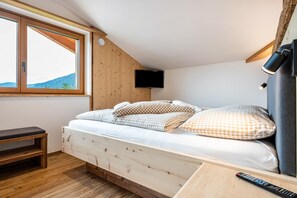 Une chambre avec un lit en bois, un banc, une télévision et une fenêtre donnant sur les montagnes.