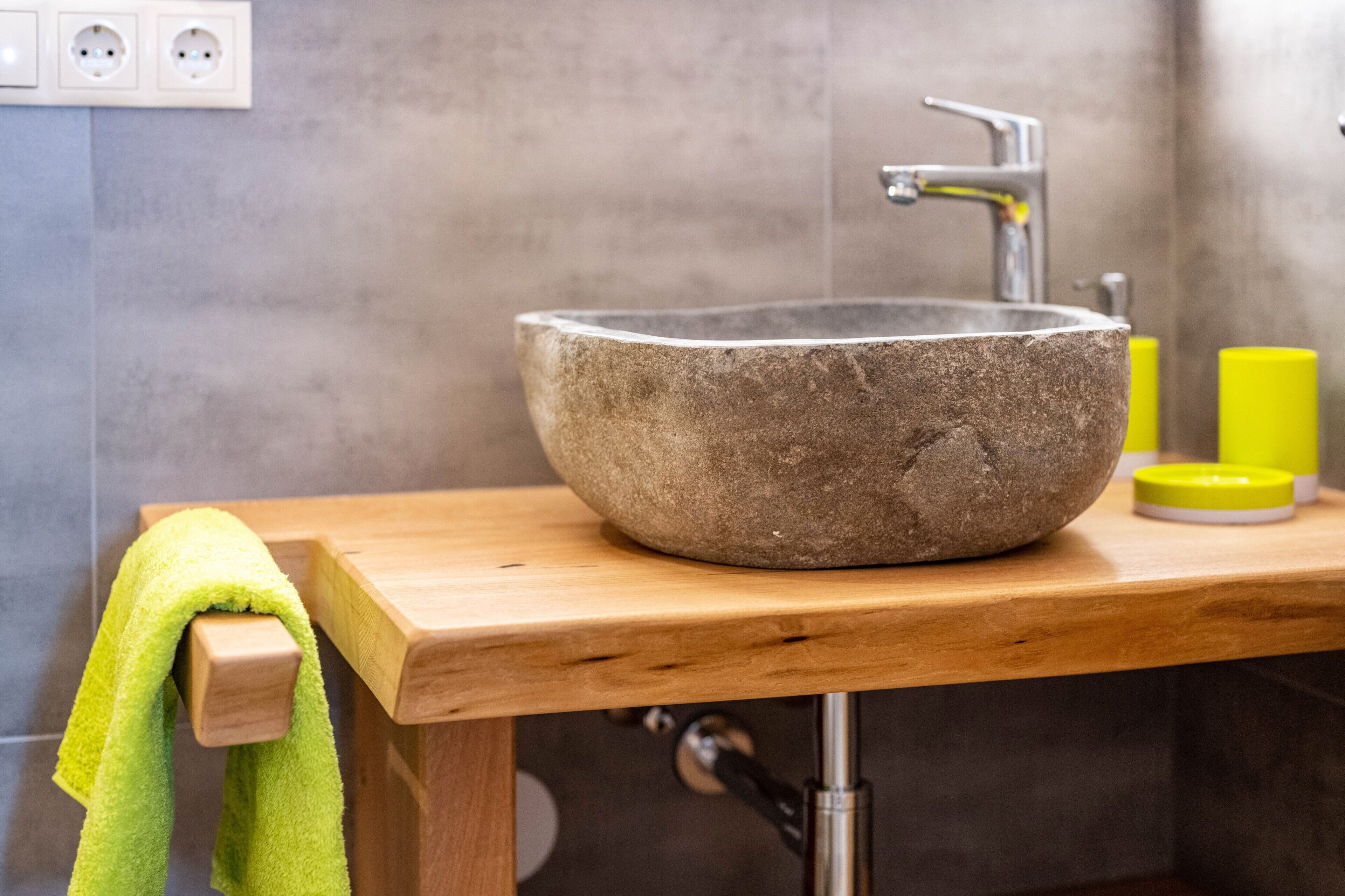 A stone sink on a wooden countertop with a towel hanging on a hook, a faucet, and a yellow container on the right.