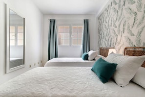 A bedroom with two beds, a window with curtains, a mirror, and a patterned wall.