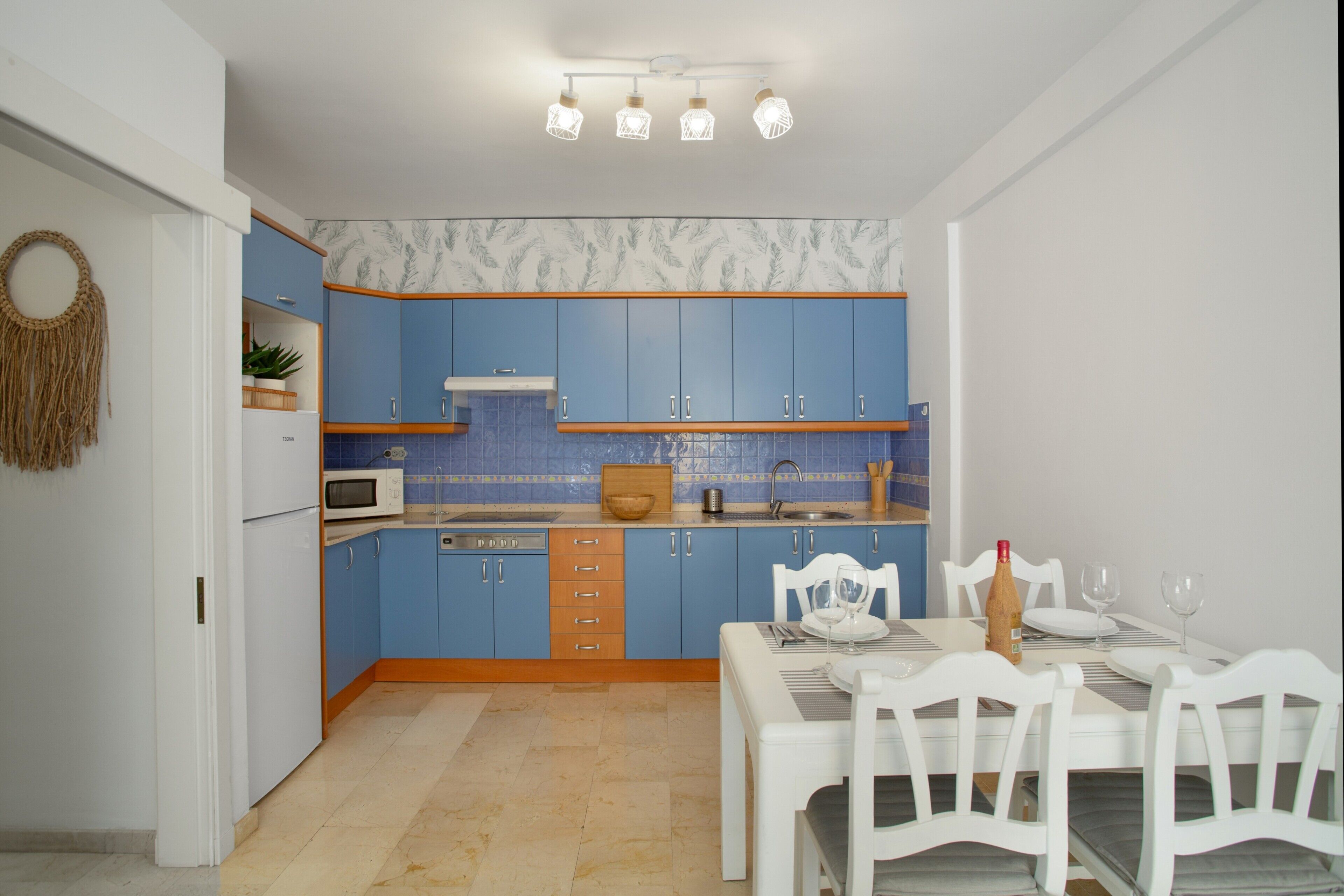 A kitchen with blue cabinets, a white refrigerator, a microwave, and a dining area with a table set for two.
