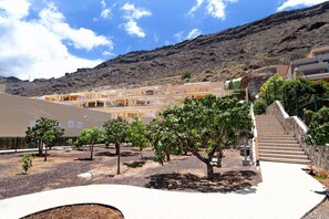 A courtyard with a staircase leading to a building, surrounded by trees and a mountainous backdrop.