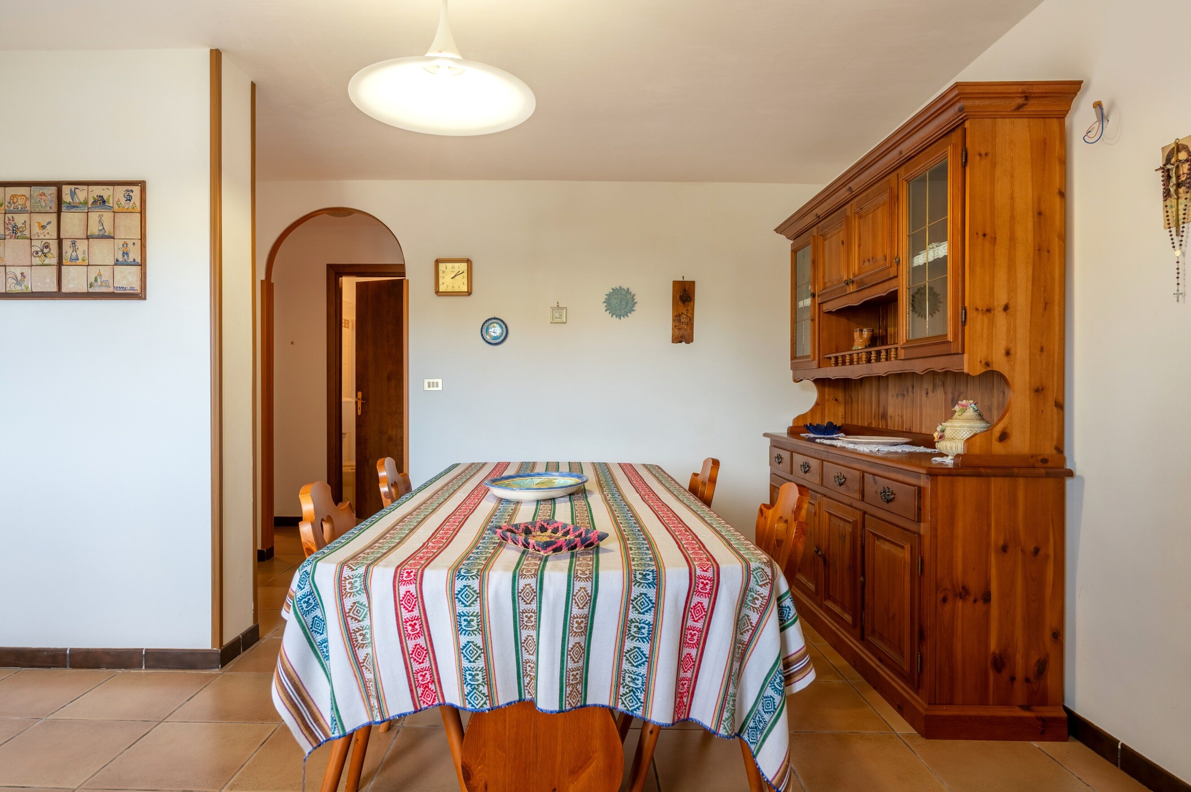 A dining area with a table set for four, a wooden cabinet with glass doors, and a hanging light fixture.