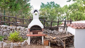 Un four en pierre installé à l’extérieur, doté d’une structure en bois, entouré d’un mur en pierre et d’une clôture en bois.