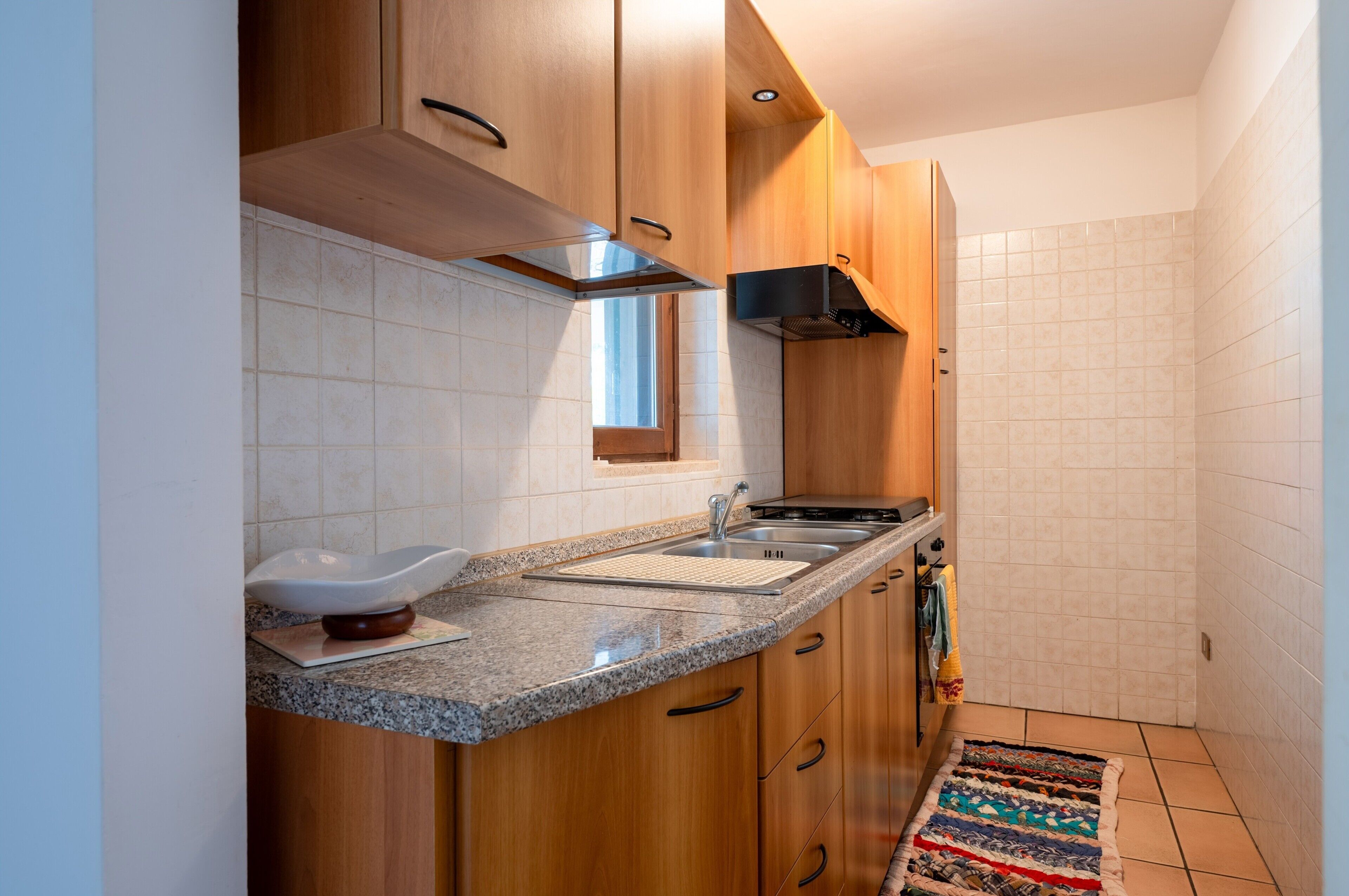 Une cuisine compacte dotée de meubles en bois, d’un plan de travail en granit, d’un évier en acier inoxydable et d’une hotte intégrée.