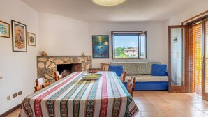 Un coin repas agrémenté d’une cheminée en pierre, d’une longue table recouverte d’une nappe colorée et d’un canapé avec des coussins bleus.
