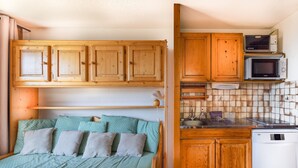 Un dormitorio pequeño con cama, armarios de madera, microondas y una kitchenette.